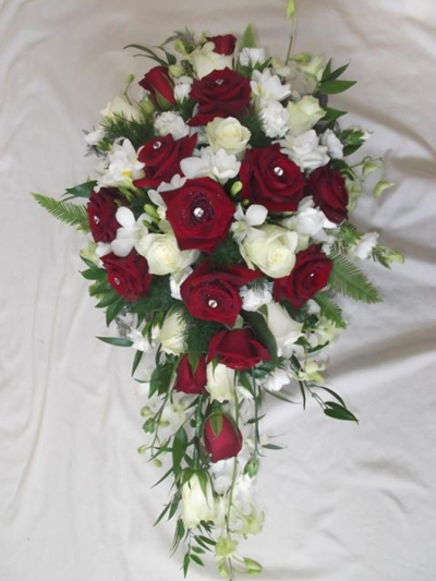 Rose & Orchid Shower Bridal Bouquet - Red Naomi roses with diamantee pins, white avalanche rose, White singapore orchids, white freesia fern anf soft ruscus trailing shower bridal bouquet Handcrafted by our Birmingham florists, this Rose & Orchid Shower Bridal Bouquet brings considered colour, texture and natural detail to a wedding day. Each piece is arranged to feel natural and polished, with textures selected to complement the chosen wedding atmosphere. Fresh materials are selected according to quality and supply, with though...